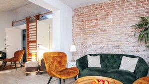 A modern living room with a brick wall, a green sofa, a wooden coffee table with fruit, and a wooden ladder. - Elegant Blavand Getaway- By Traum Ferienwohnungen (Blavand)
