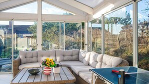A sunlit room with a large window, a sofa, a table with a vase of flowers, and a ping pong table. - Elegant Blavand Getaway- By Traum Ferienwohnungen (Blavand)