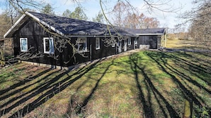 A large, single-story wooden building with a sloped roof, surrounded by a grassy area with shadows cast by trees. - 4 Person Holiday Park Home in Laeso (Læsø)