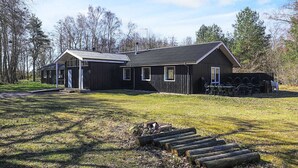 A black building with a sloped roof, a covered porch, and a small outdoor seating area with tables and chairs. - 6 Person Holiday Park Home in Laeso (Læsø)