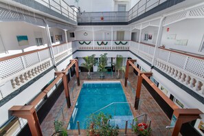 Una piscina interior de varios niveles con una escalera central, rodeada de balcones con barandillas y plantas en macetas.