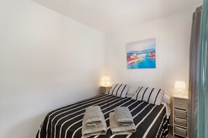 Habitación de hotel con una cama, dos lámparas de noche, un cuadro en la pared y una ventana con cortinas.