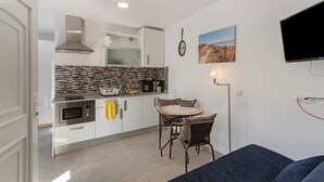 Een compacte keuken met een magnetron, broodrooster en koffiezetapparaat, een eethoek met rieten stoelen, een plafondventilator en een flatscreen televisie aan de muur.