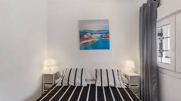 Een slaapkamer met een bed, twee nachtkastjes met lampen, een schilderij aan de muur en een raam met gordijnen.