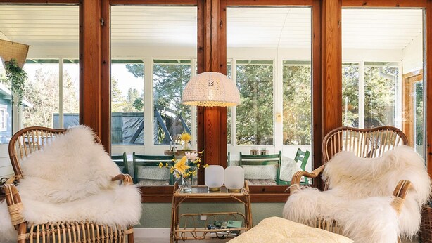 A cozy room with wicker furniture, a table with a vase of flowers, and large windows offering a view of the outdoors. - 6 Person Holiday Home in Vaeggerlose (Vaeggerlose)