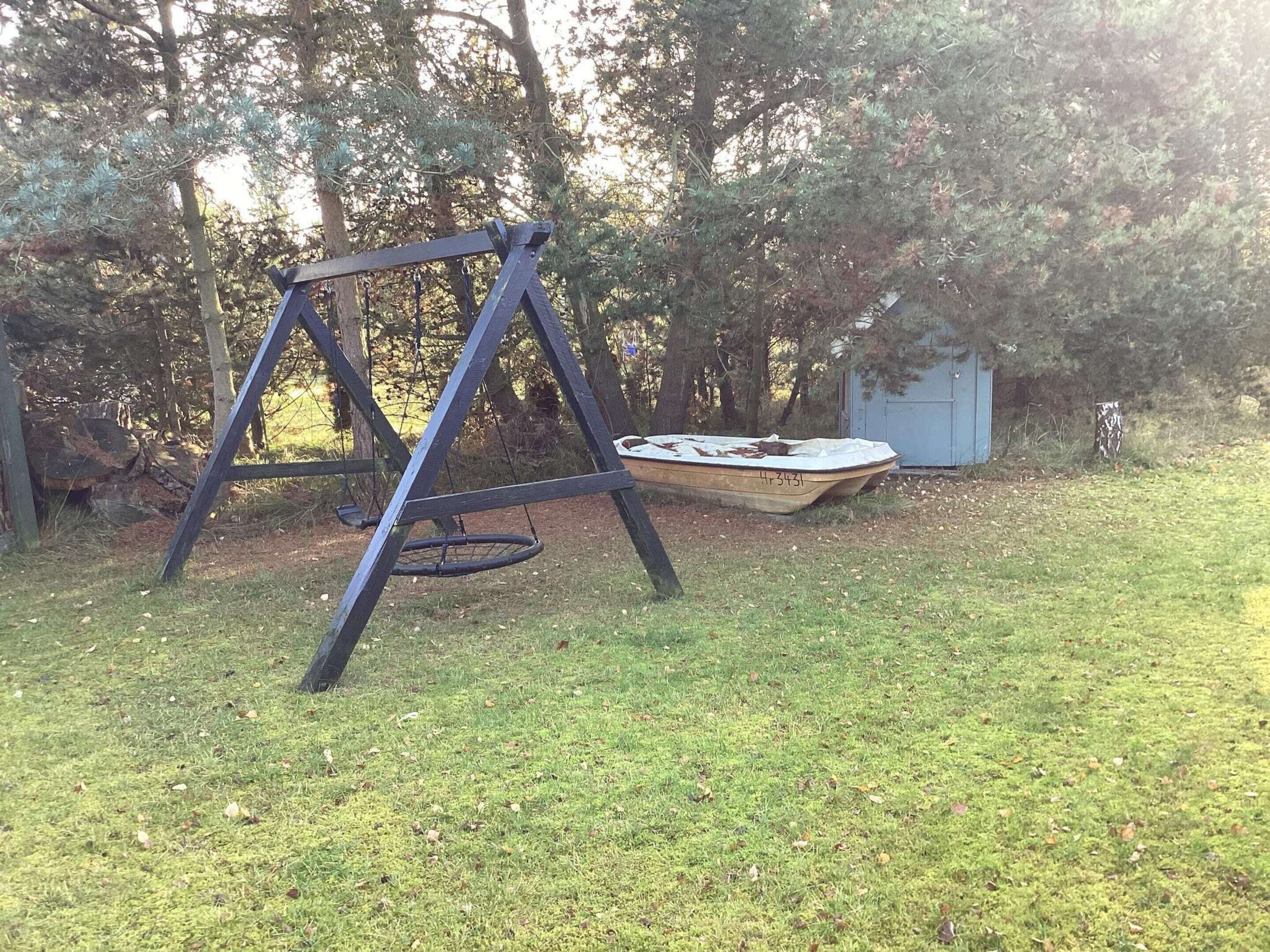 Een schommel in een gazon, met een klein bootje en een tuinhuis op de achtergrond.