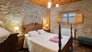 A room with a stone wall, wooden ceiling, a bed with a wooden headboard, two bedside tables with lamps, and a window with shutters. - Rural House 'Cal Panxeta' with Mountain Views, Wi-Fi and Air Conditioning (Balsareny)