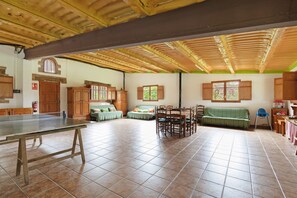 A spacious room with a ping pong table, wooden cabinets, a dining table with chairs, and a green sofa.