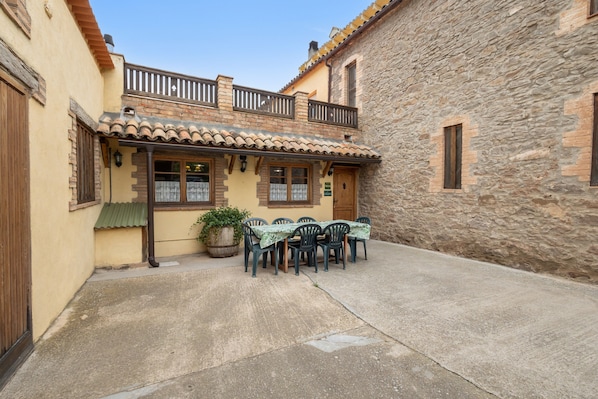 A courtyard with a table and chairs, a potted plant, and a building with a balcony.