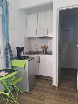 Une cuisine compacte avec des meubles blancs, une machine à café, un évier et une petite table avec une chaise.