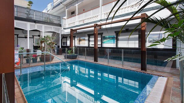 An indoor swimming pool with a clear view of the surrounding architecture, including a balcony and a staircase. - Vacation Studio 'Paula- 23' with Mountain View, Shared Pool and Wi-Fi (Arinaga)