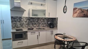 A compact kitchen with a microwave, stove, and coffee maker, a small dining table with chairs, and a clock on the wall. - Vacation Studio 'Paula- 23' with Mountain View, Shared Pool and Wi-Fi (Arinaga)