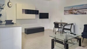 A modern living room with a glass coffee table, a dining area with chairs, a flat-screen TV mounted on the wall, a ceiling fan, and a painting on the wall. - Vacation Studio 'Paula- 23' with Mountain View, Shared Pool and Wi-Fi (Arinaga)