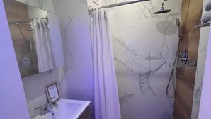 A modern bathroom with a marble wall, a shower with a handheld showerhead, a toilet, and a vanity with a sink and mirror.