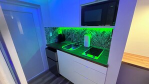 A compact kitchen with a microwave, sink, and a green-lit backsplash.