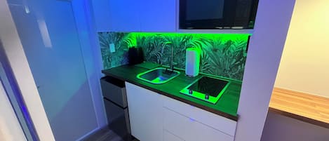 Cocina compacta con microondas, pileta y un salpicadero iluminado en verde.