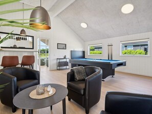 Un salon moderne doté d’une table de billard, de sièges confortables, d’un téléviseur et offrant une vue sur la verdure environnante.