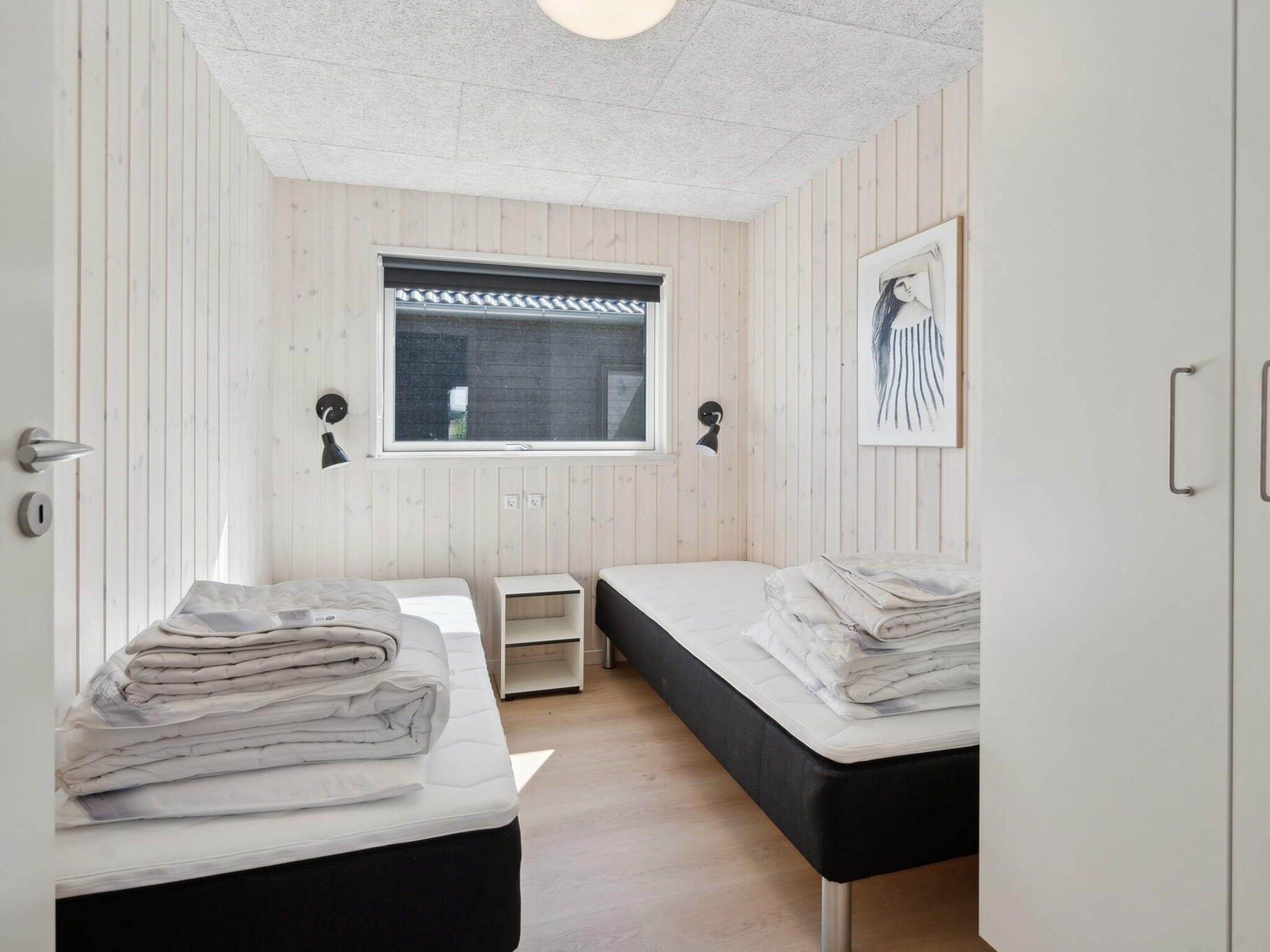 A bedroom with two beds, a window with blinds, a bedside lamp, and a framed picture on the wall.