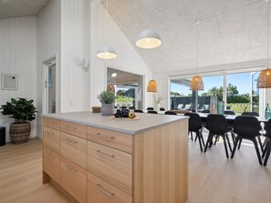 Een moderne keuken met een centraal eiland, houten kastjes en een eethoek met zwarte stoelen en een groot raam met uitzicht op het omliggende landschap.