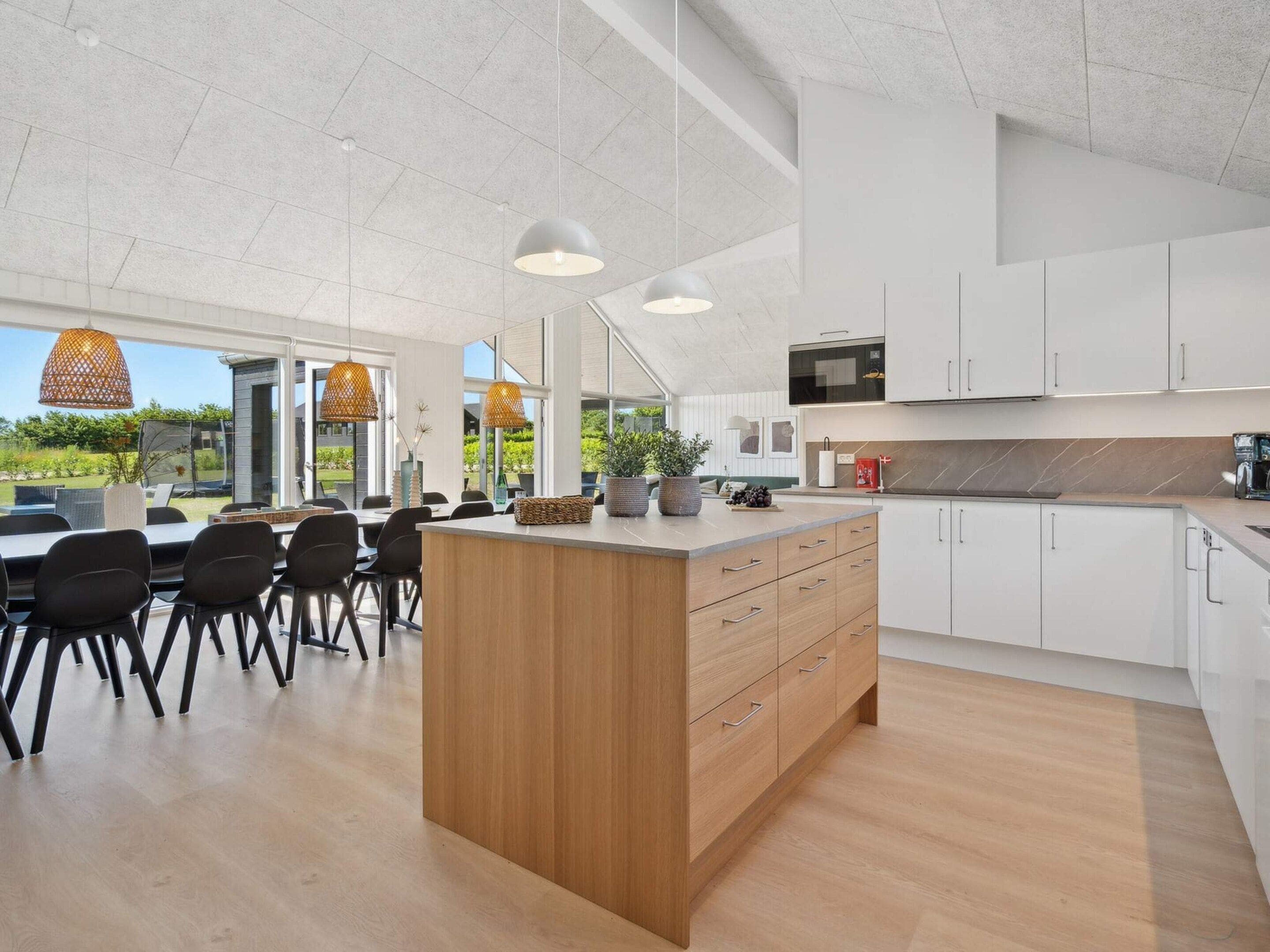 Una cocina moderna con armarios blancos, una isla de madera e iluminación colgante.