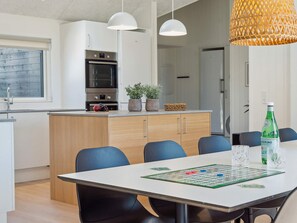Une cuisine moderne avec un coin repas, comprenant une table sur laquelle est disposé un jeu de société, des chaises et une bouteille d’eau.
