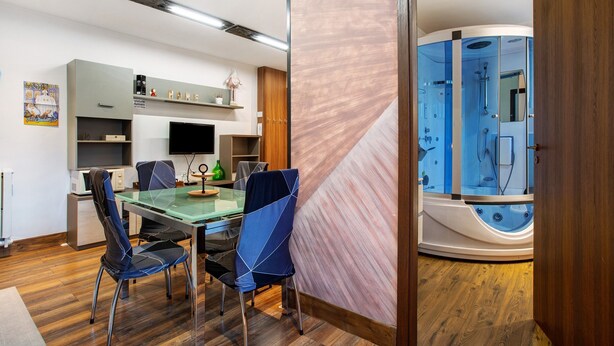 A modern room with a glass table, chairs, a flat-screen TV, a wooden cabinet, and a visible shower area. - Apartment 'Buthier' with Mountain View, Balcony and Wi-Fi (Aosta)