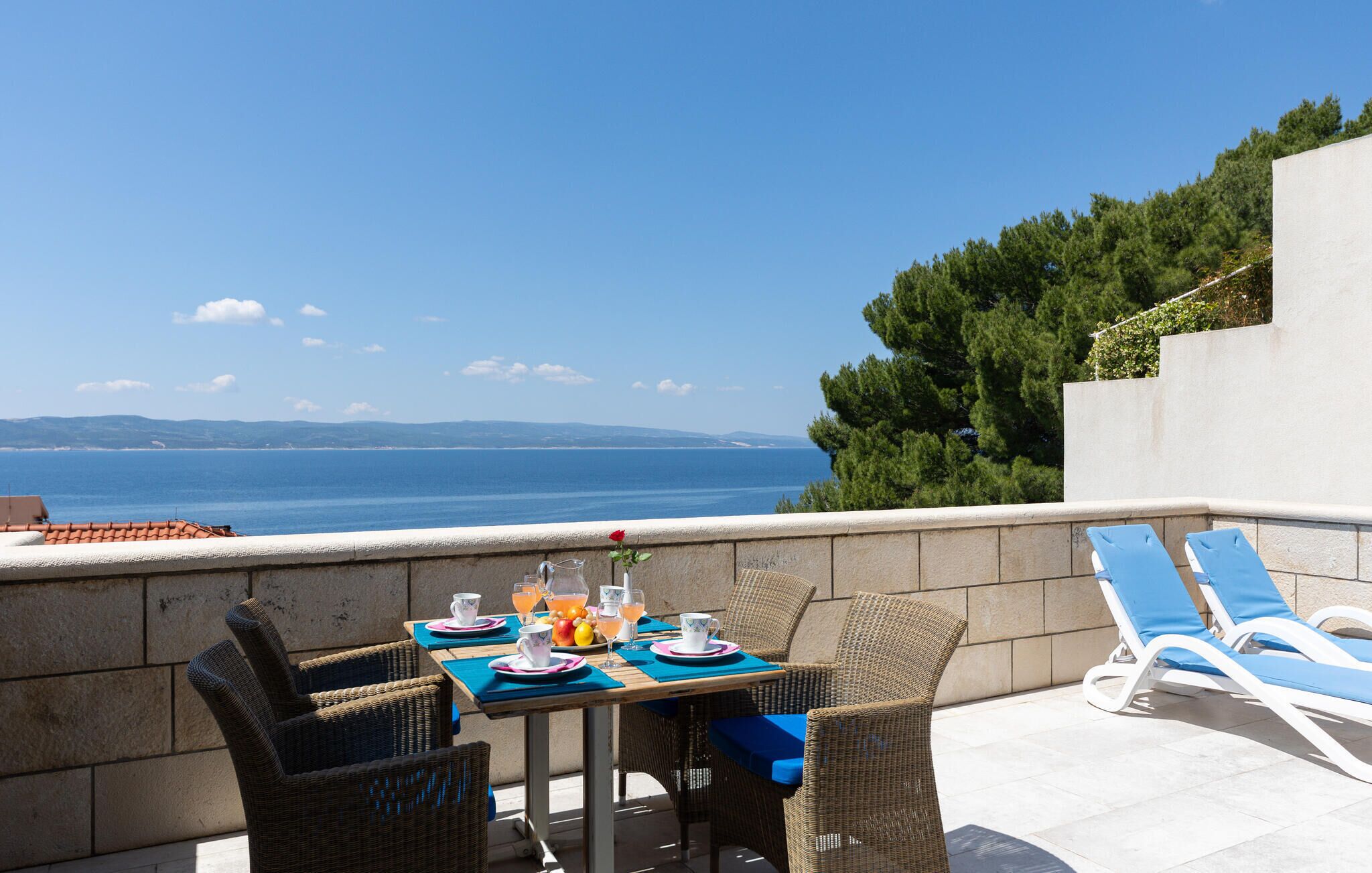 A terrace with wicker furniture, a table set with plates, cups, and glasses, and a view of the sea.