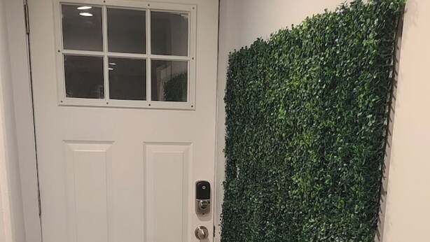 Un couloir avec une porte blanche, un mur vert orné de motifs de feuillage et un sol carrelé.