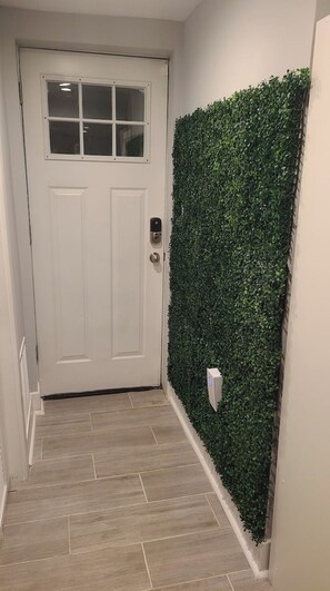 A hallway with a white door, a green wall with foliage, and a tiled floor. - Cozy Basement Suite with Outdoor Oasis in NE Washington, DC! (Washington)