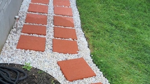 Un chemin de jardin bordé de carreaux rouges et blancs, entouré de pelouse et d’une clôture en bois.