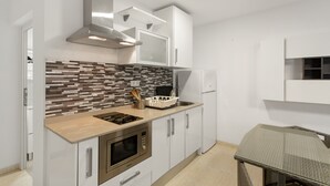 Una cocina moderna con armarios blancos, salpicadero de azulejos, horno empotrado y una mesa con cubierta de vidrio.