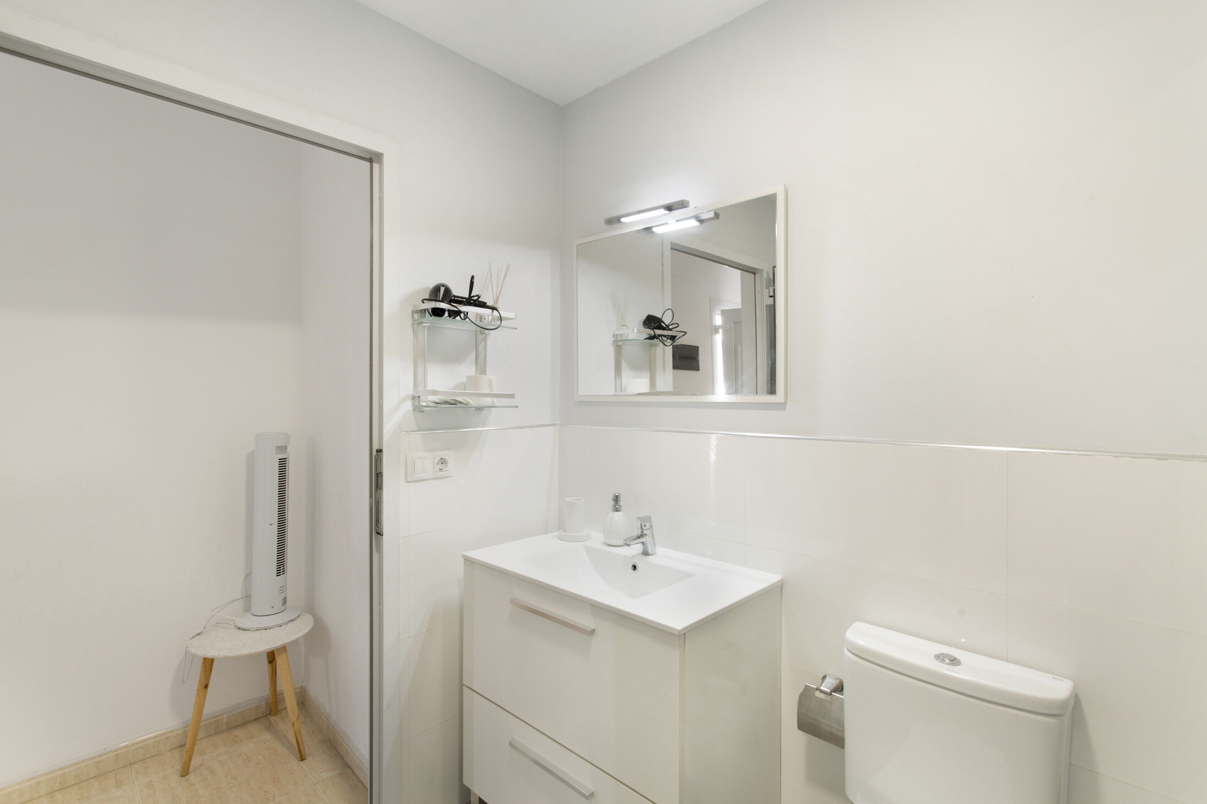 Un bagno con un mobile lavabo bianco, uno specchio, un WC e un piccolo tavolo con una ventola.