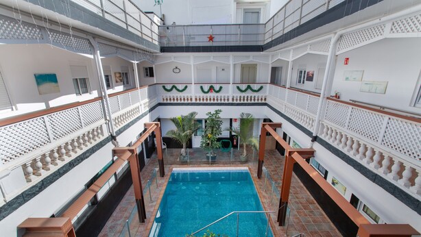 Una piscina interior de varios niveles con una escalera central, rodeada de balcones con barandillas y plantas en macetas.