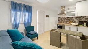 Una sala moderna con sofá, una silla, una mesa de comedor y una cocina con armarios y microondas.