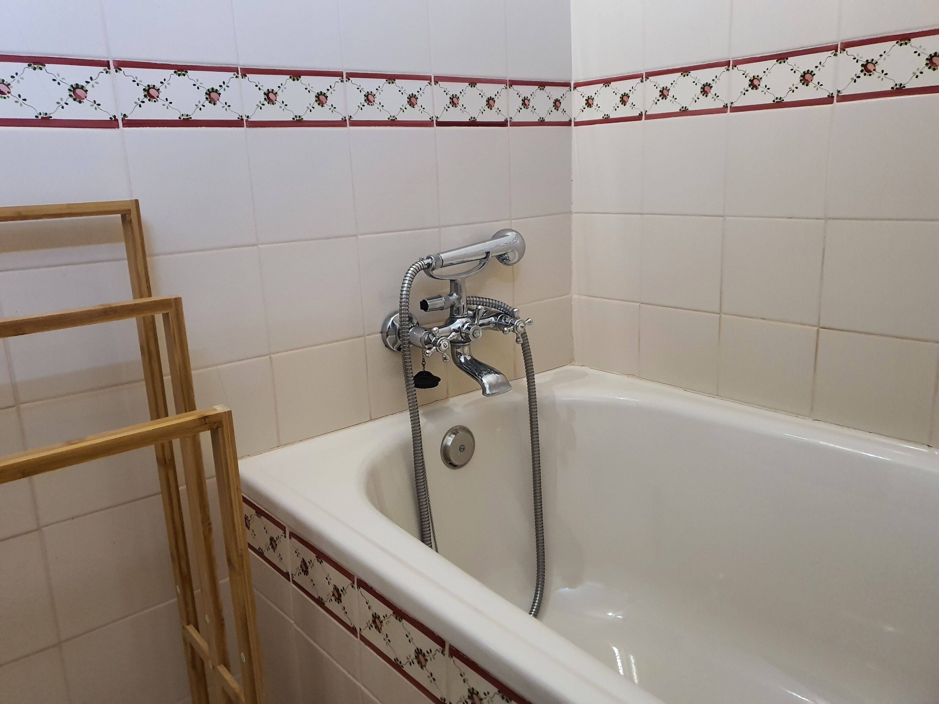 A bathroom with a bathtub, a wooden ladder, and decorative floral tiles.
