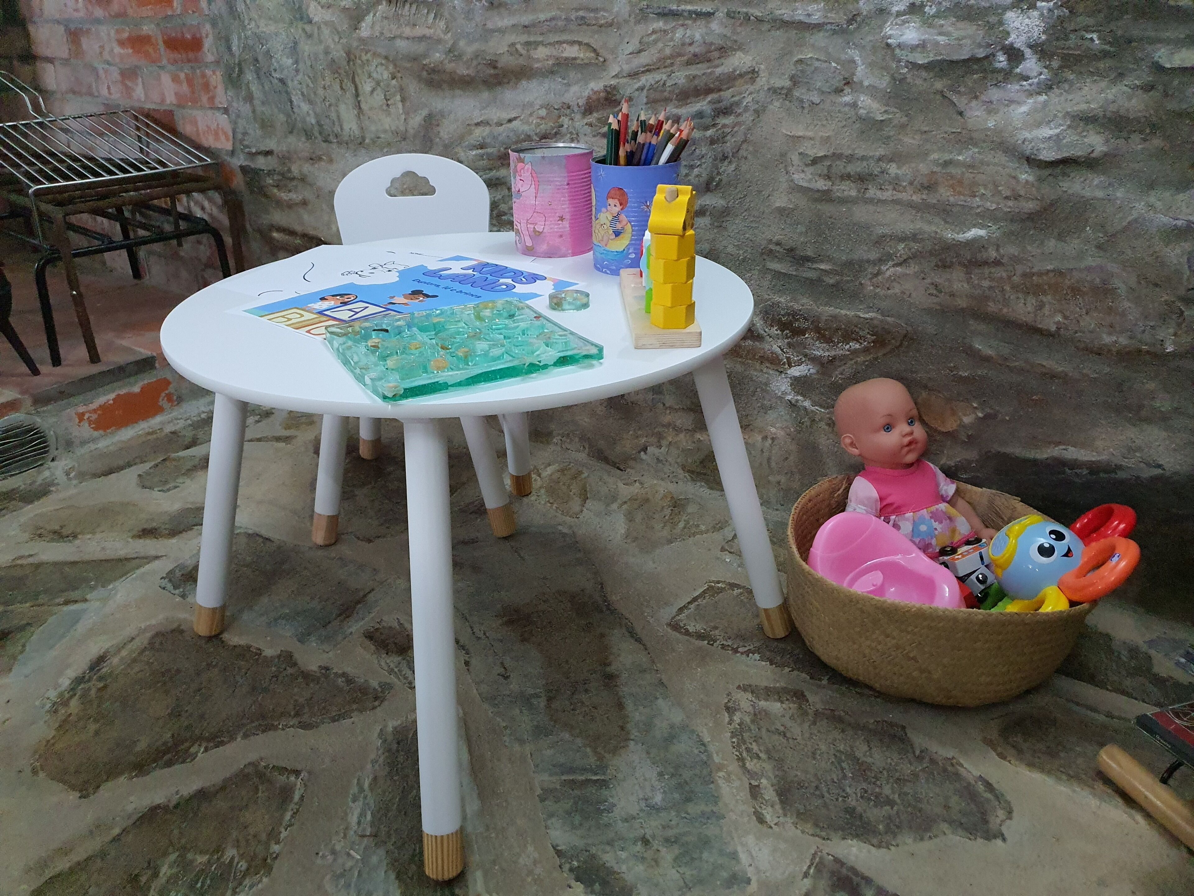 Una mesa con un libro infantil, un coche de juguete y una cesta con una muñeca y juguetes.