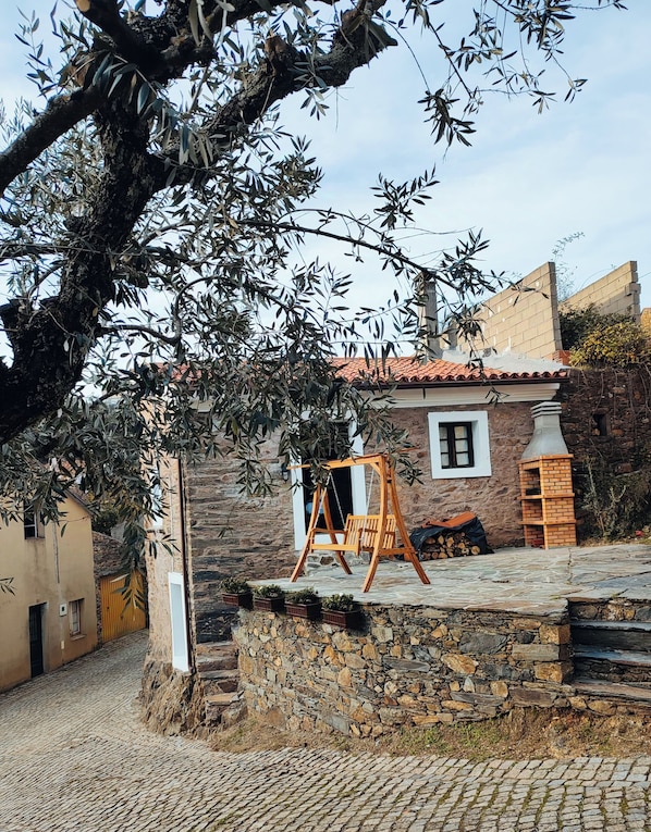Un edificio de piedra con un columpio de madera en el frente, un muro de piedra y un tejado de tejas.