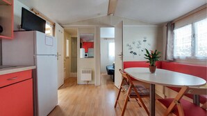 Eine kompakte Küche mit Kühlschrank, Mikrowelle und Spüle. Es gibt einen Essbereich mit Tisch und Stühlen, und ein Fenster mit einer Pflanze darauf.
