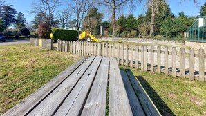 Eine hölzerne Bank in einem Park mit einer gelben Rutsche und einem umzäunten Bereich.