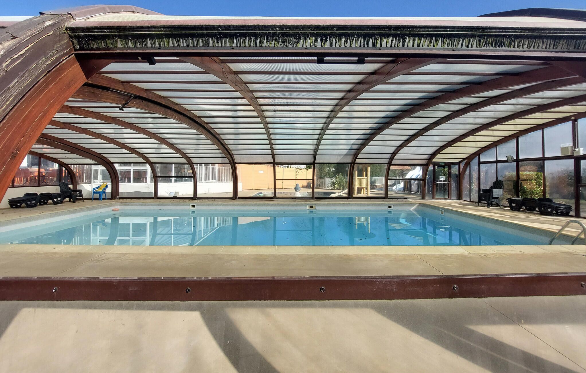 En inomhuspool med ett välvt tak, väggar av genomskinligt glas och ett betonggolv.