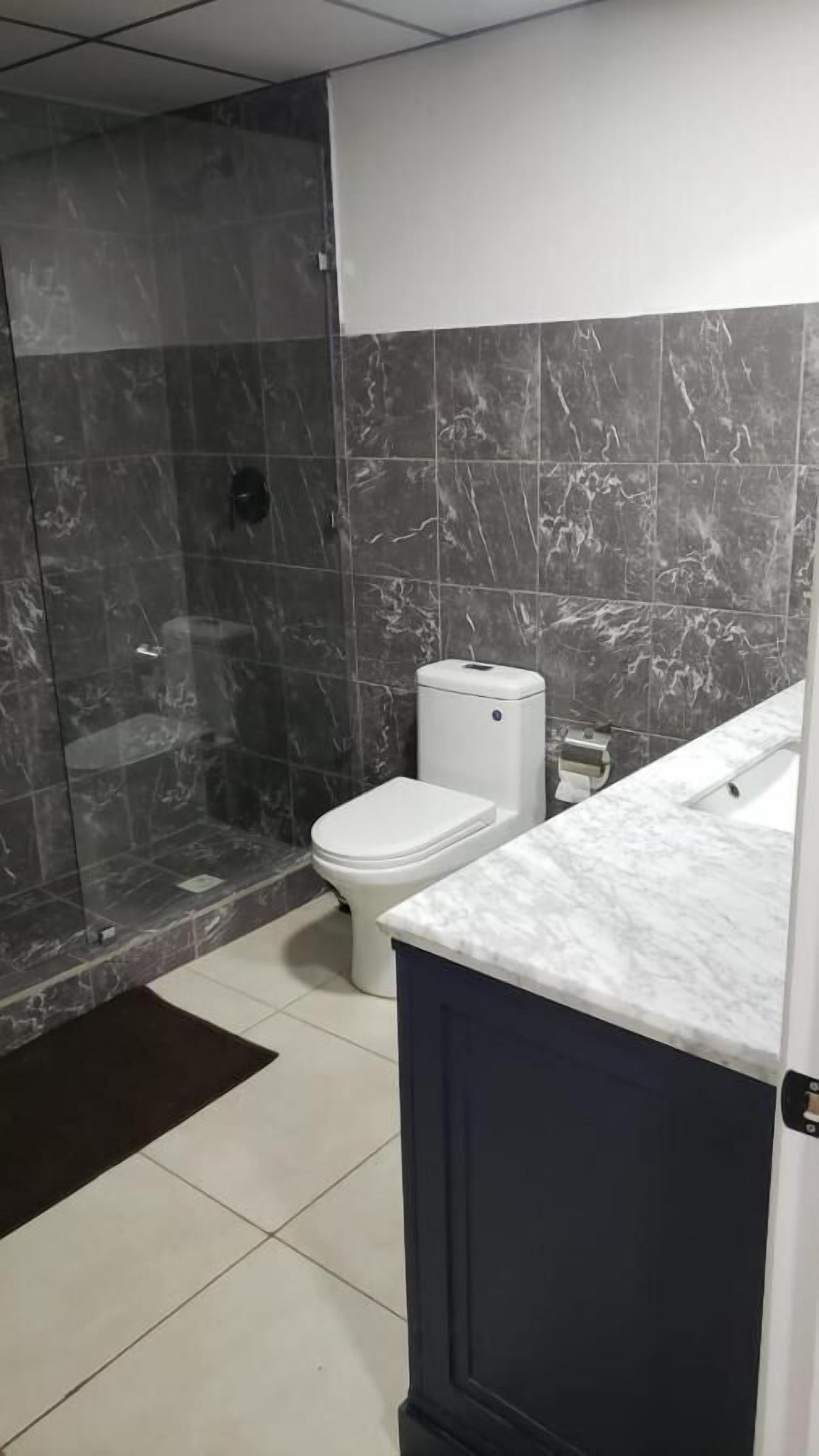 A bathroom with a shower, toilet, and marble-tiled walls.