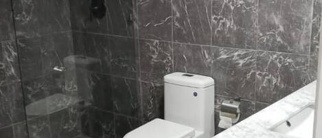 A bathroom with a shower, toilet, and marble-tiled walls.