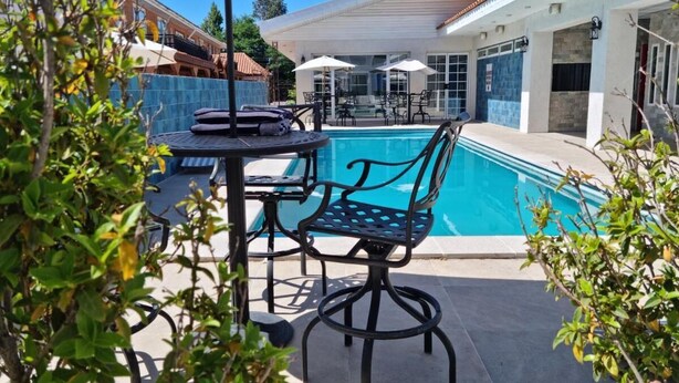 Una zona de piscina con mesa y sillas, rodeada de una terraza con baldosas y un porche cubierto.