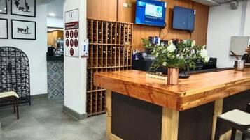 A reception area with a wooden counter, a television mounted on the wall, and a wine rack in the background.