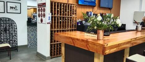 A reception area with a wooden counter, a television mounted on the wall, and a wine rack in the background.