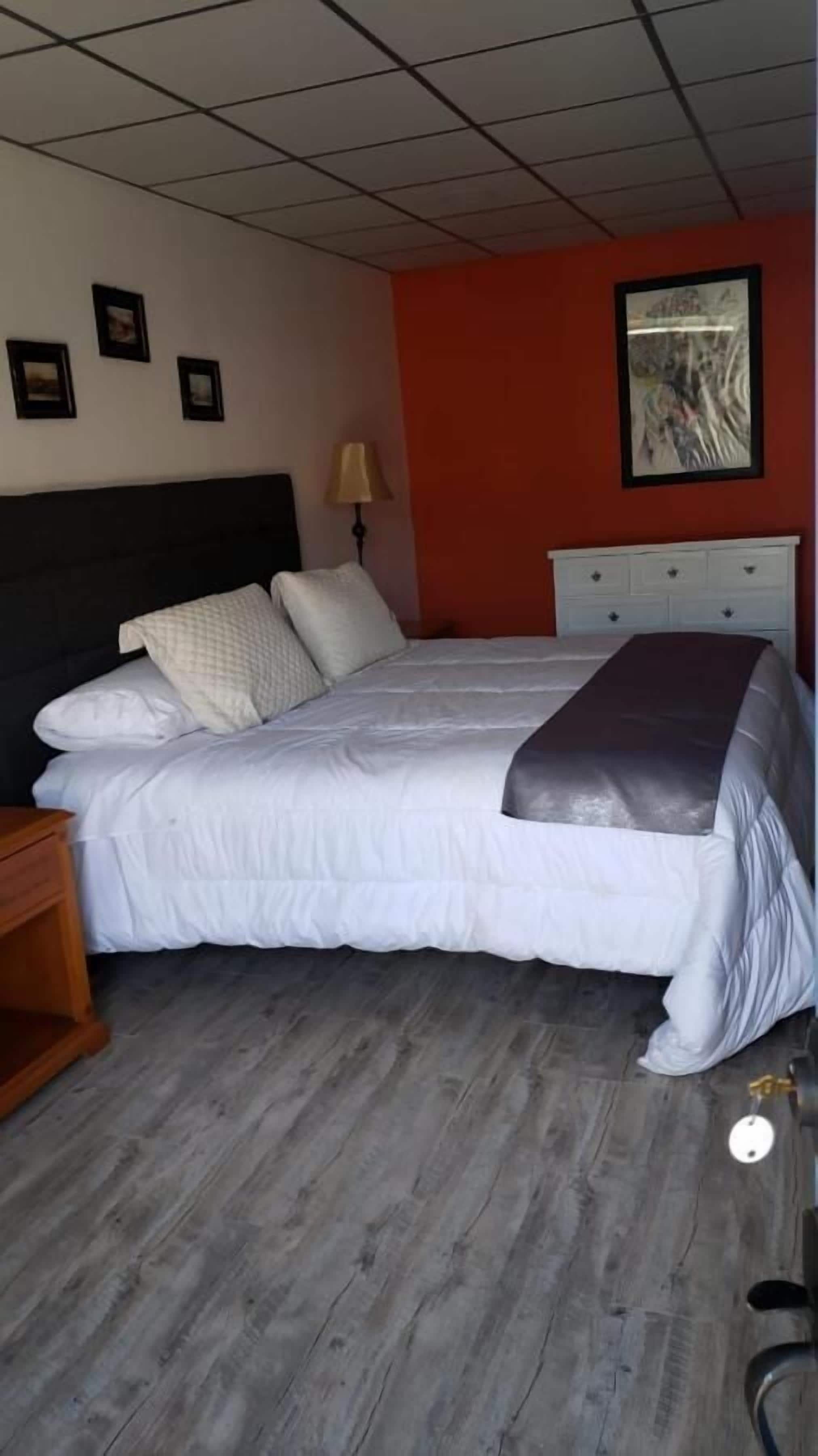 A bedroom with a bed, a nightstand, a lamp, a dresser, and a framed picture on the wall.