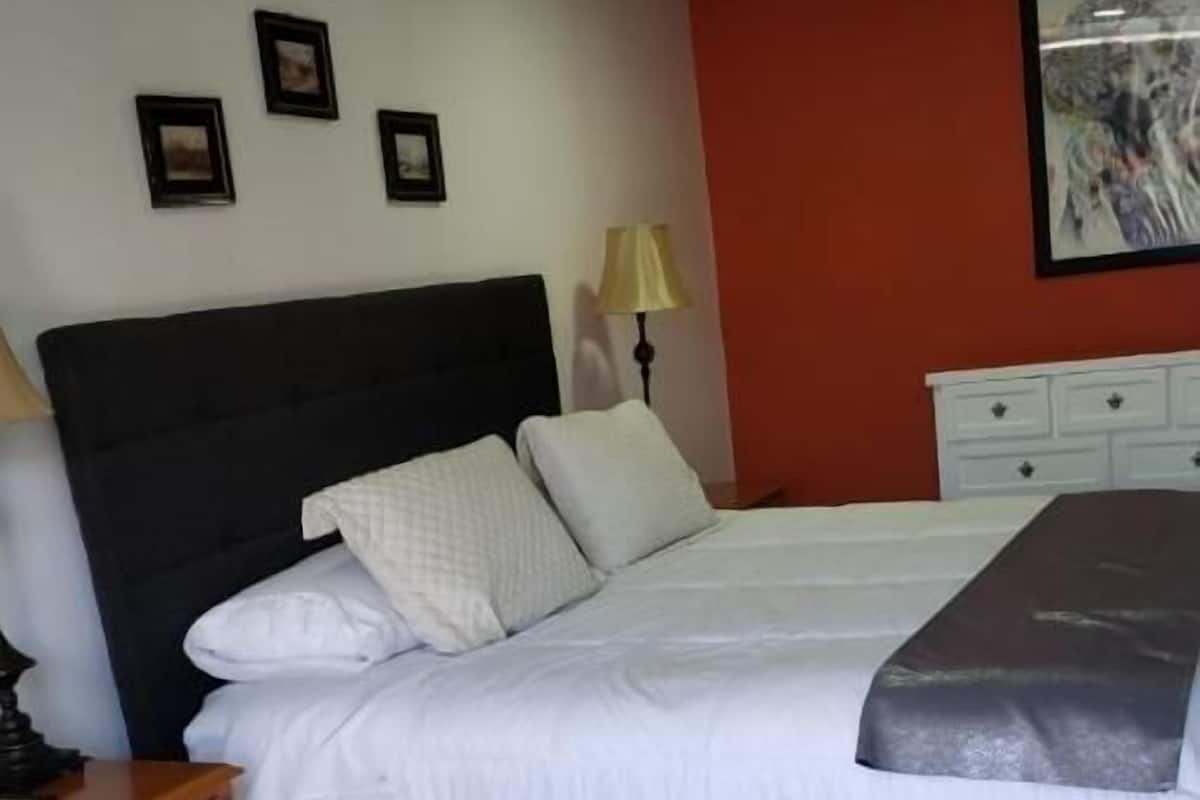 Een slaapkamer met een bed, nachtkastje, dressoir en een schilderij aan de muur.