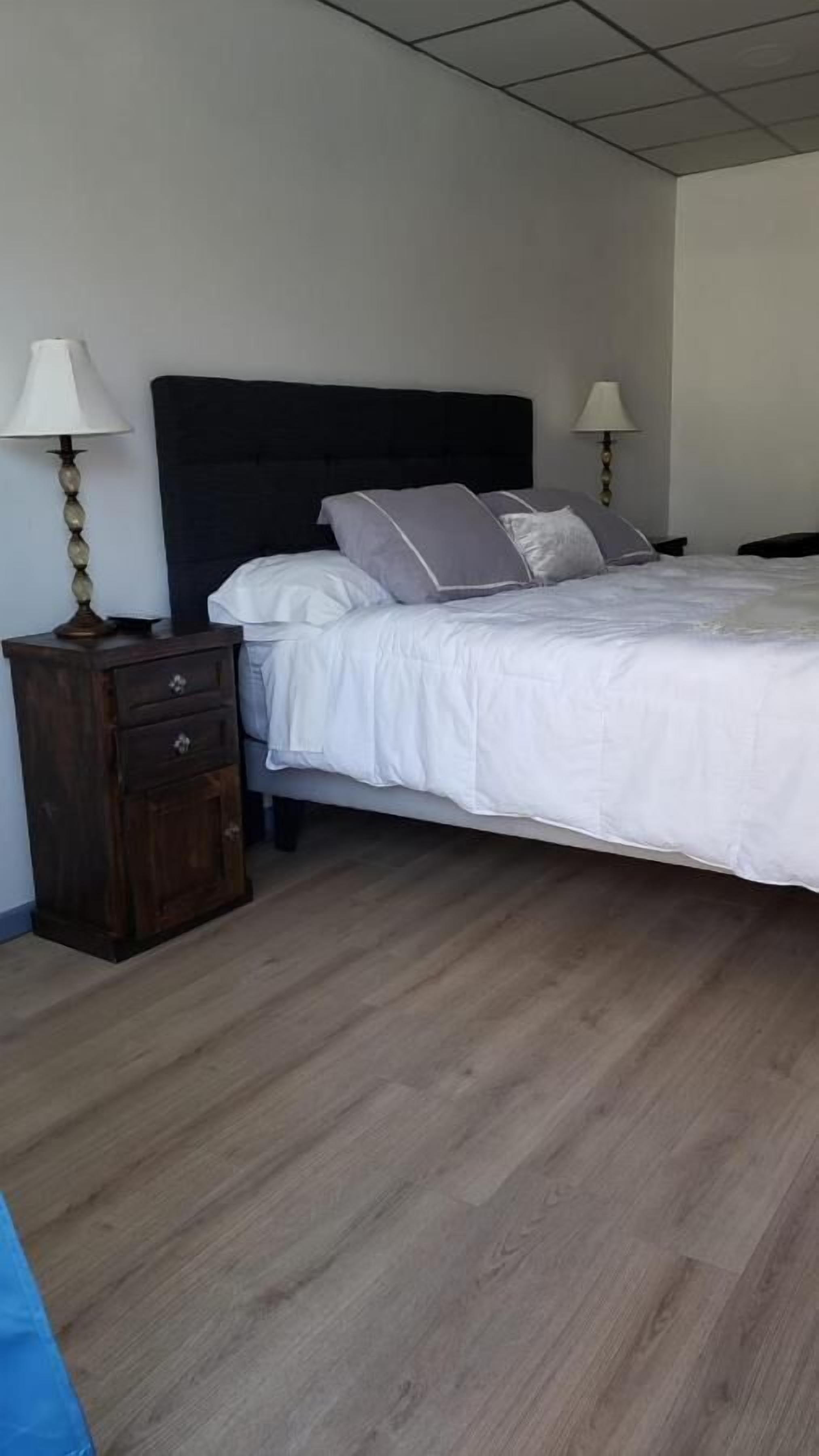 A bedroom with a bed, two bedside tables, a wooden nightstand, and a lamp.