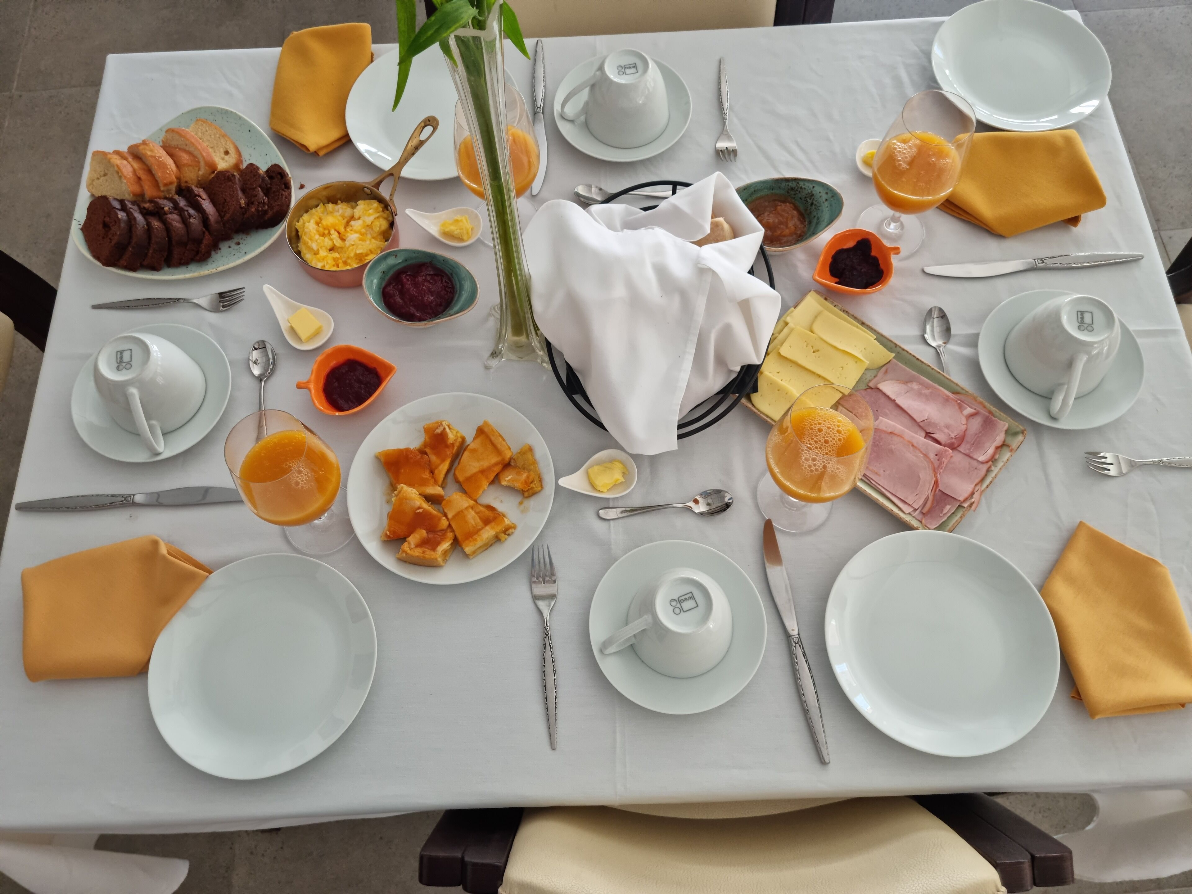 Una mesa de desayuno con platos de comida, cubiertos y un florero.
