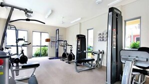Une salle de sport équipée de divers appareils d’exercice, dotée de grandes fenêtres et d’un ventilateur de plafond.